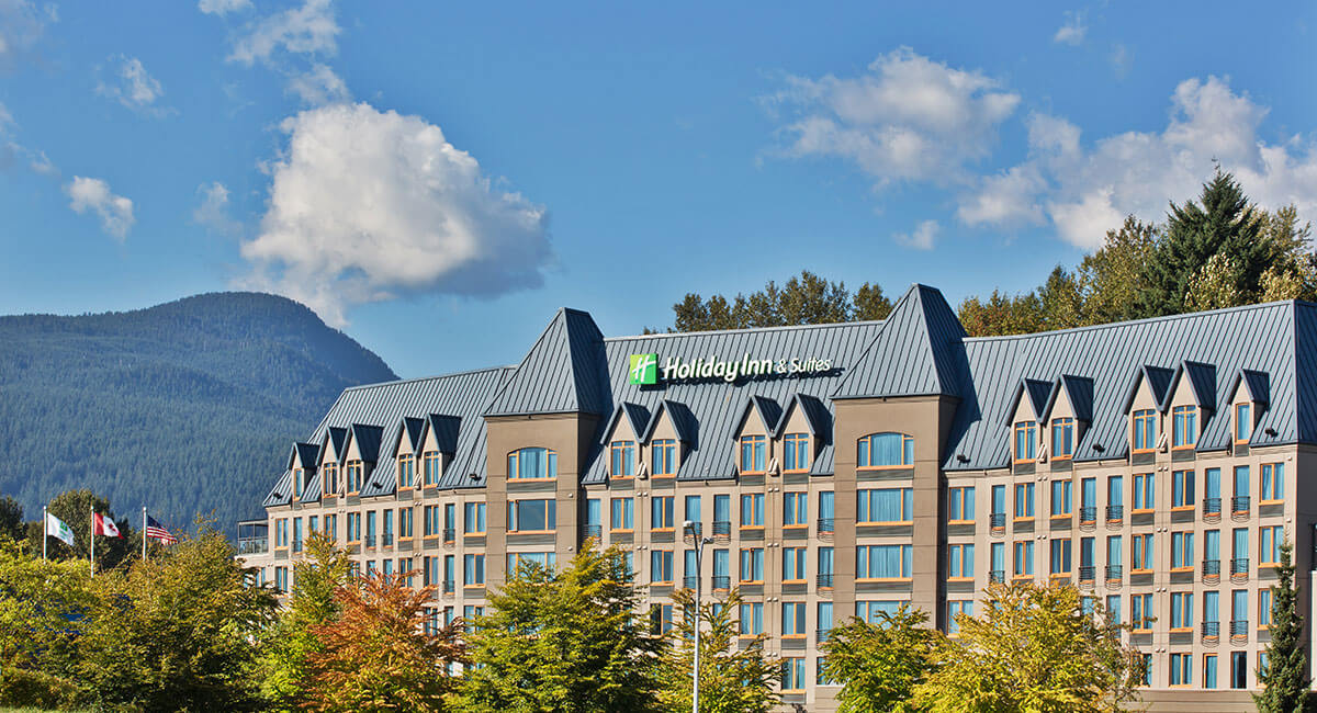 Holiday Inn North Vancouver against the backdrop of blue sky, mountains and trees