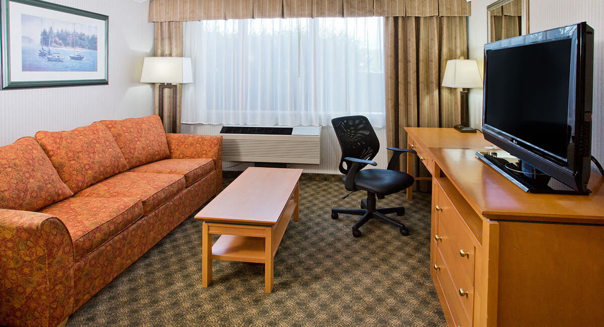 Room with spacious couch, desk, coffee table and TV at Holiday Inn North Vancouver