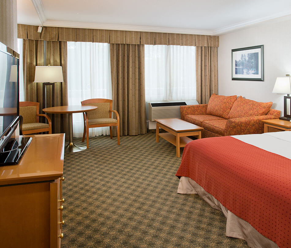 Single queen room furnished with tables, lamps and chairs at the Holiday Inn North Vancouver