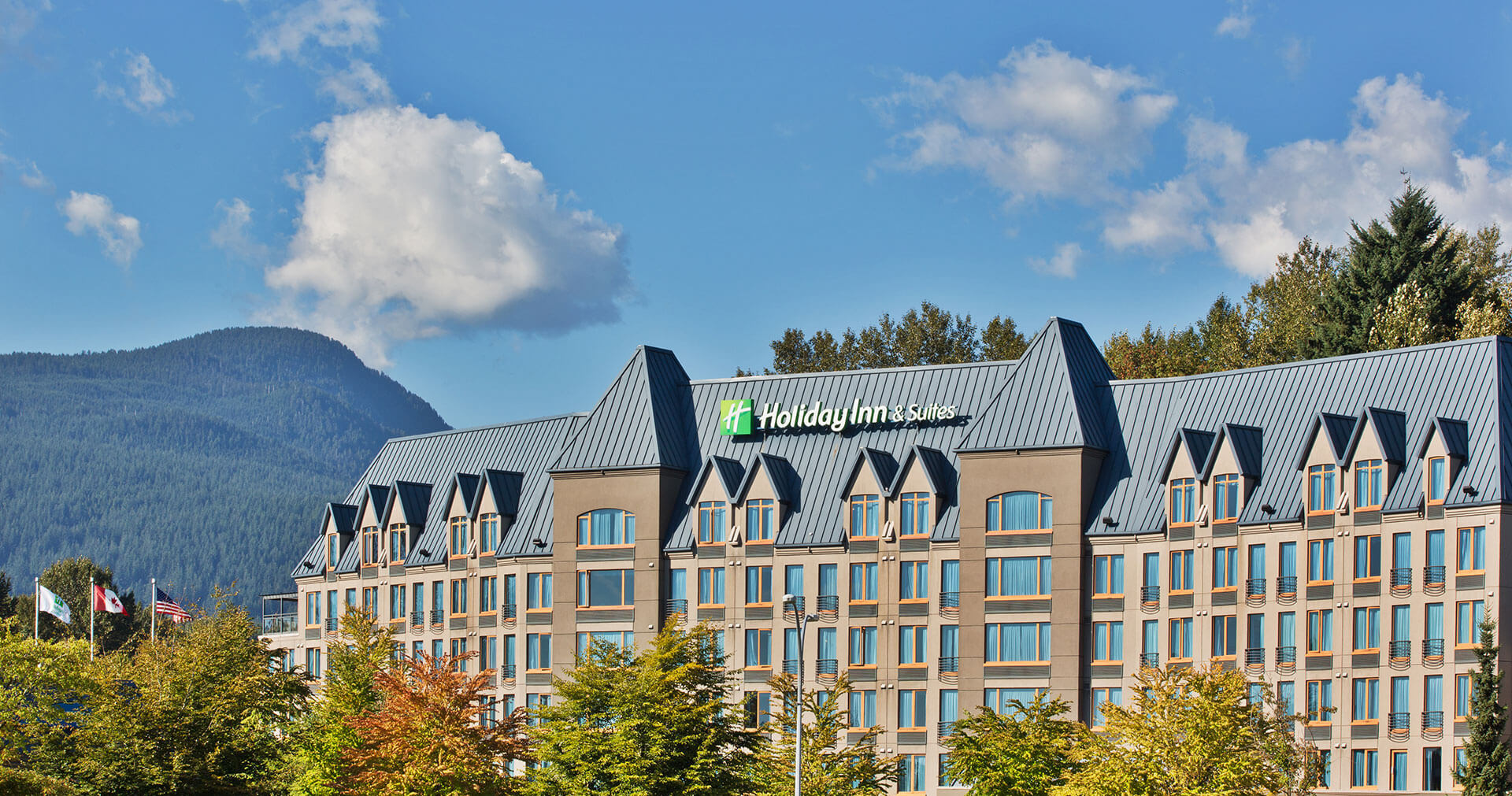 Holiday Inn North Vancouver surrounded by blue skies, trees and mountains